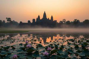 A serene sunrise over Angkor Wat, ancient temple silhouettes reflected in a tranquil lotus pond, lush greenery surrounding the site, soft morning mist enveloping the scene, a peaceful atmosphere evoking mindfulness and meditation.